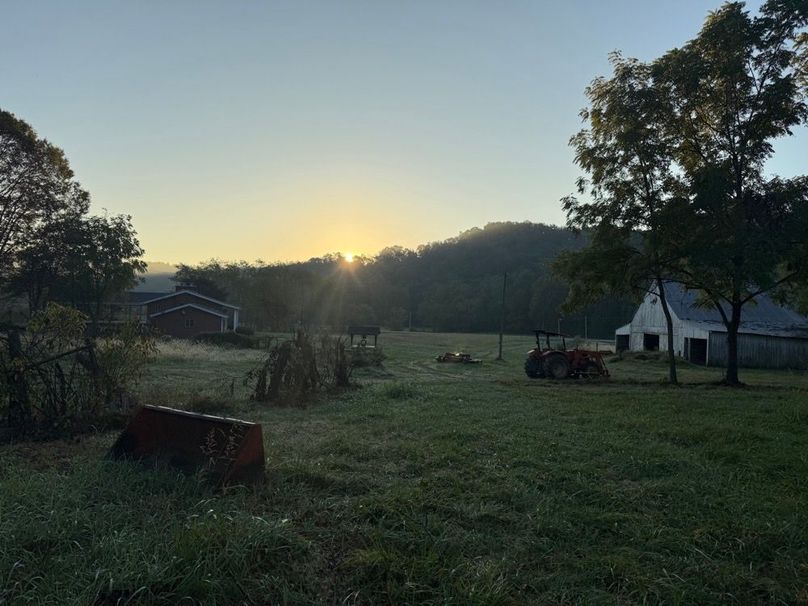 006 Peaceful morning light settles over the farmstead, highlighting open pasture, mature trees, and a quiet country setting.